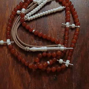 May include: A brown and white prayer beads with a silver tassel. The beads are strung on a brown cord and the tassel is made of silver wire. The beads are arranged in a circle and the tassel is hanging down from the center of the circle. The beads are made of a smooth, polished material and the tassel is made of a shiny, metallic material. The beads are a traditional Islamic prayer accessory.