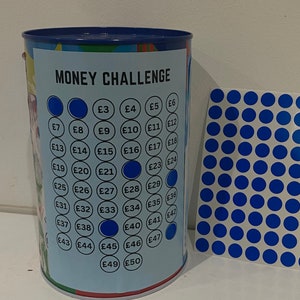 May include: A blue and white money challenge jar with a grid of numbers from 3 to 50. The jar has a blue lid and a blue sticker with the words "MONEY CHALLENGE" on it. The jar is filled with blue stickers that have numbers on them.