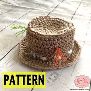 May include: A crocheted brown hat with a wide brim and various colored yarn accents. The hat is on a white wooden surface. The text "PATTERN" is in black letters on a yellow background.
