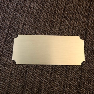 May include: A gold-colored metal plaque with rounded corners. The plaque is blank and ready for engraving.