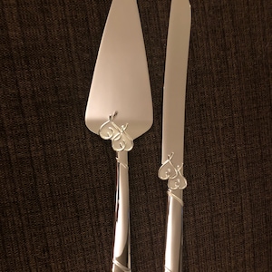 May include: A silver wedding cake knife set with two intertwined hearts on each handle.