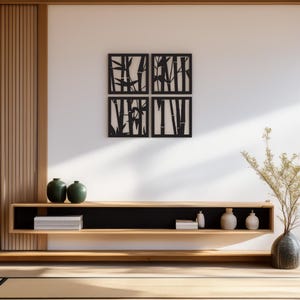 May include: Four square black bamboo wall art panels are mounted on a white wall. Below, a wooden shelf displays green vases, small white boxes, and decorative ceramic pieces. A vase with dried plants sits on the floor.
