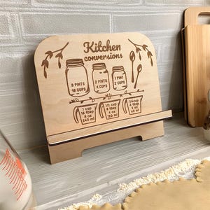 May include: Wooden kitchen conversions chart with engraved text and illustrations. The chart displays measurements for pints, cups, tablespoons, and ounces. The text reads "Kitchen conversions".