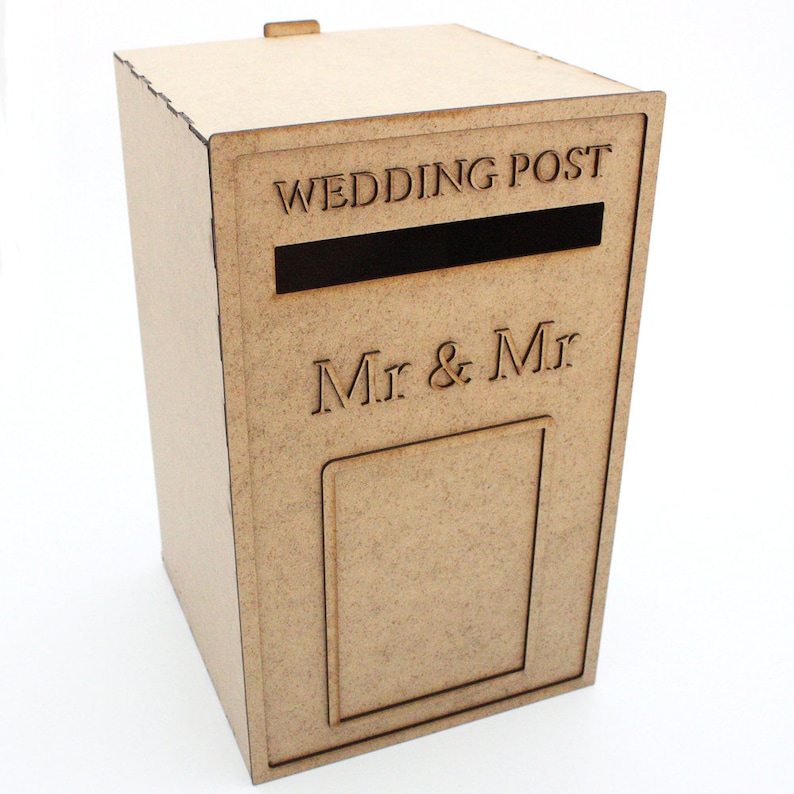 May include: A light brown wooden wedding post box with the words "WEDDING POST" and "Mr & Mr" engraved on the front. The box has a slot for cards and a small door. A small wooden tab is on top.