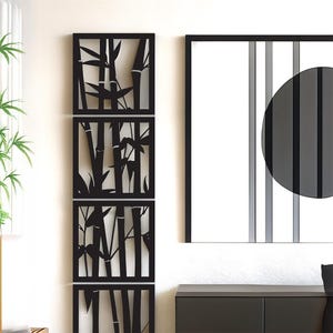 May include: Black metal wall art featuring a bamboo design. The art is composed of three rectangular panels stacked vertically, each with a cut-out bamboo silhouette. A framed artwork with a black circle and vertical stripes is also visible.