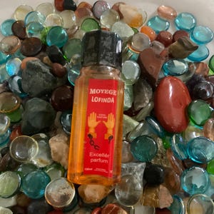 Pu&ograve; includere: Una bottiglia di vetro trasparente con un tappo nero riempita di liquido arancione. La bottiglia &egrave; etichettata "Moy&egrave;ge Lofinda Excell&eacute;r parfum 150ml". La bottiglia &egrave; circondata da pietre di vetro colorate.