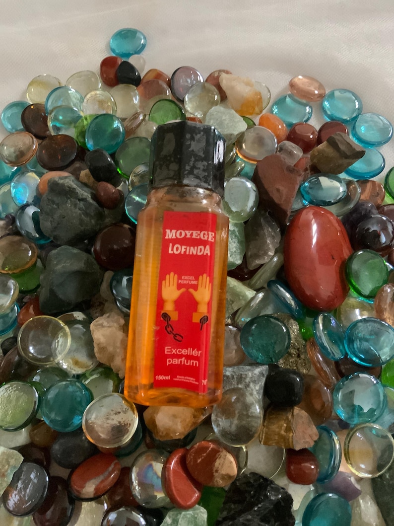 Pu&ograve; includere: Una bottiglia di vetro trasparente con un tappo nero riempita di liquido arancione. La bottiglia &egrave; etichettata "Moy&egrave;ge Lofinda Excell&eacute;r parfum 150ml". La bottiglia &egrave; circondata da pietre di vetro colorate.