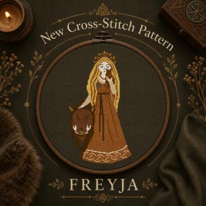 Op de afbeelding: Een kruissteekpatroon in een ronde houten borduurring met een figuur met lang haar, een kroon en een bruine jurk, naast een bruin everzwijn. De tekst New Cross-Stitch Pattern en FREYJA staat in het wit op de donkere achtergrond.