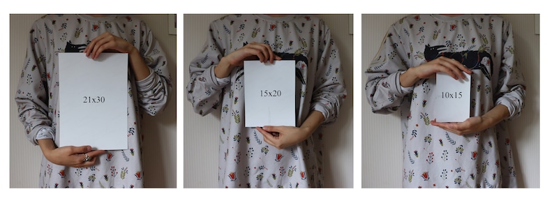May include: Three white cards with black text showing different sizes: 21x30, 15x20, and 10x15. The cards are held by a person wearing a gray and white patterned shirt.