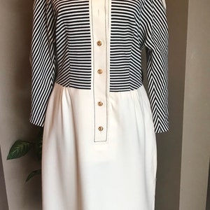 May include: A white and black striped dress with a white bottom half and gold buttons. The dress has a high collar and long sleeves.