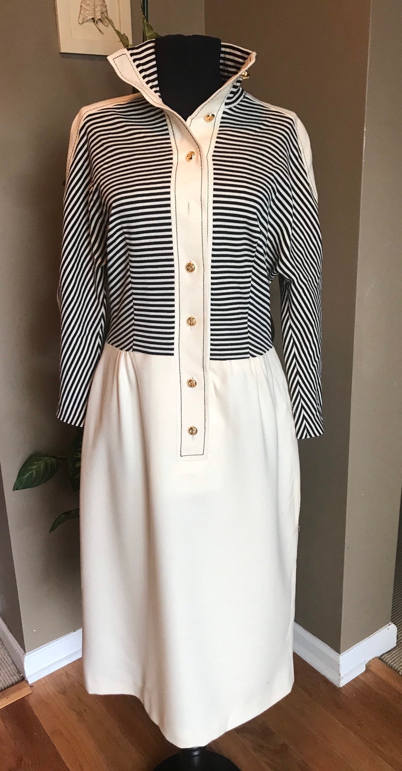 May include: A white and black striped dress with a white bottom half and gold buttons. The dress has a high collar and long sleeves.