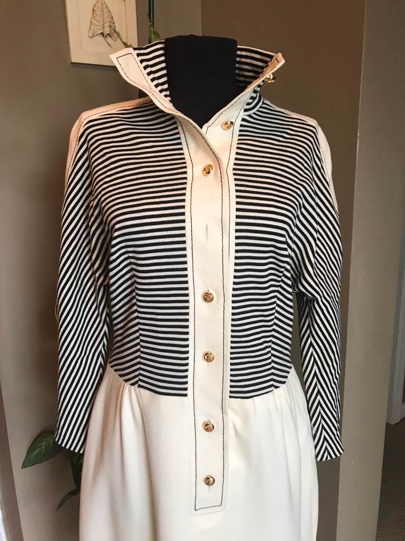 May include: A white and black striped long-sleeved dress with a white bottom half and gold buttons down the front.
