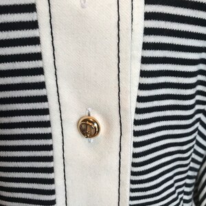 May include: Close-up of a white and black striped shirt with two gold buttons. The buttons have an anchor design.
