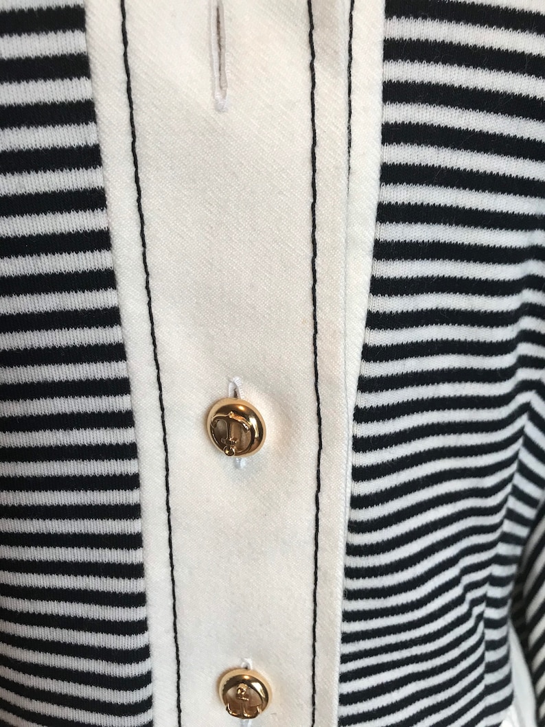 May include: Close-up of a white and black striped shirt with two gold buttons. The buttons have an anchor design.