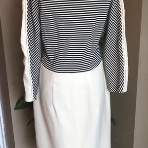 May include: A white dress with a black and white striped bodice and a white skirt. The dress has long sleeves and a high neckline.