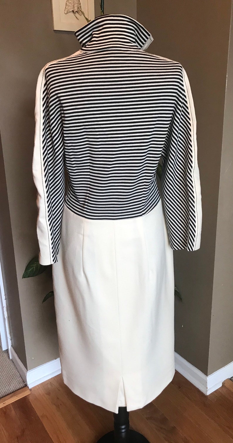 May include: A white dress with a black and white striped bodice and a white skirt. The dress has long sleeves and a high neckline.