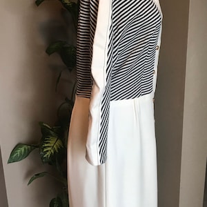 May include: A white dress with a black and white striped bodice and long sleeves. The dress has a high collar and gold buttons.