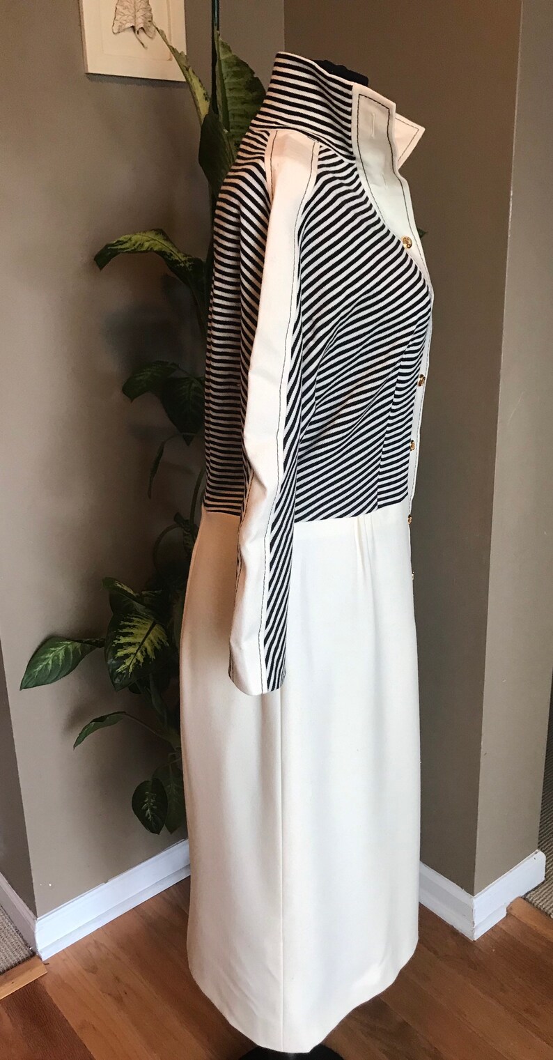May include: A white dress with a black and white striped bodice and long sleeves. The dress has a high collar and gold buttons.