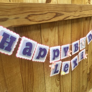 May include: A purple and white Happy Birthday banner with pink and white flowers and a bandage design. The banner reads "Happy Birthday Lexi".