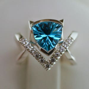 May include: A silver ring with a triangular blue topaz gemstone and a V-shaped band accented with small white diamonds.