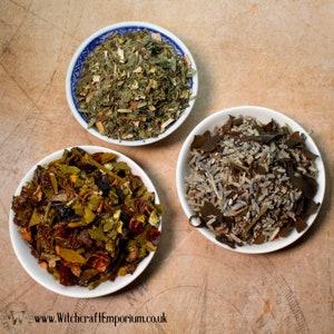 May include: Three white bowls filled with different types of dried herbs and flowers. The bowls are on a brown background with a compass design.