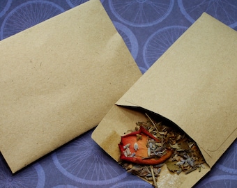 May include: Two brown paper envelopes, one with a small amount of dried herbs and a dried rose petal inside. The envelopes are on a purple background with a repeating pattern of bicycle wheels.