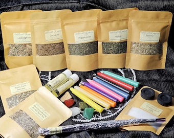Puede incluir: Una colección de hierbas secas, incienso, velas y otros suministros mágicos para la brujería y los hechizos. Los artículos están dispuestos sobre un fondo de tela azul oscuro con el texto "www.Witchcraft-Emporium.com".