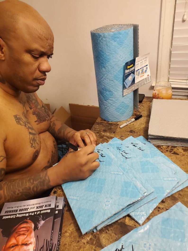May include: A person signing a stack of blue Scotch Flex & Seal tape. The tape is labeled "Scotch Flex & Seal" and has a diamond pattern. The person is signing the tape with a black marker. The book "Memoir of a Pro Wrestling Extremist: New Jack and Jason Norman" is visible in the foreground.
