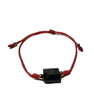 Puede incluir: Pulsera de hilo rojo con una piedra negra rectangular. La pulsera tiene cuentas doradas a ambos lados de la piedra y es ajustable. Una joya sencilla y elegante.
