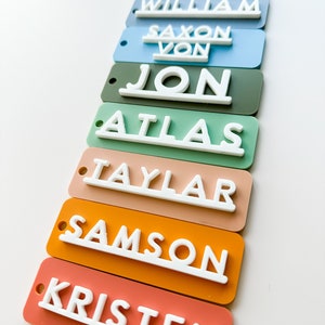 Op de afbeelding: Een set van acht kleurrijke rechthoekige naamstickers met witte letters. De namen zijn: Bennett, William, Saxon Von, Jon, Atlas, Taylar, Samson en Kristen.
