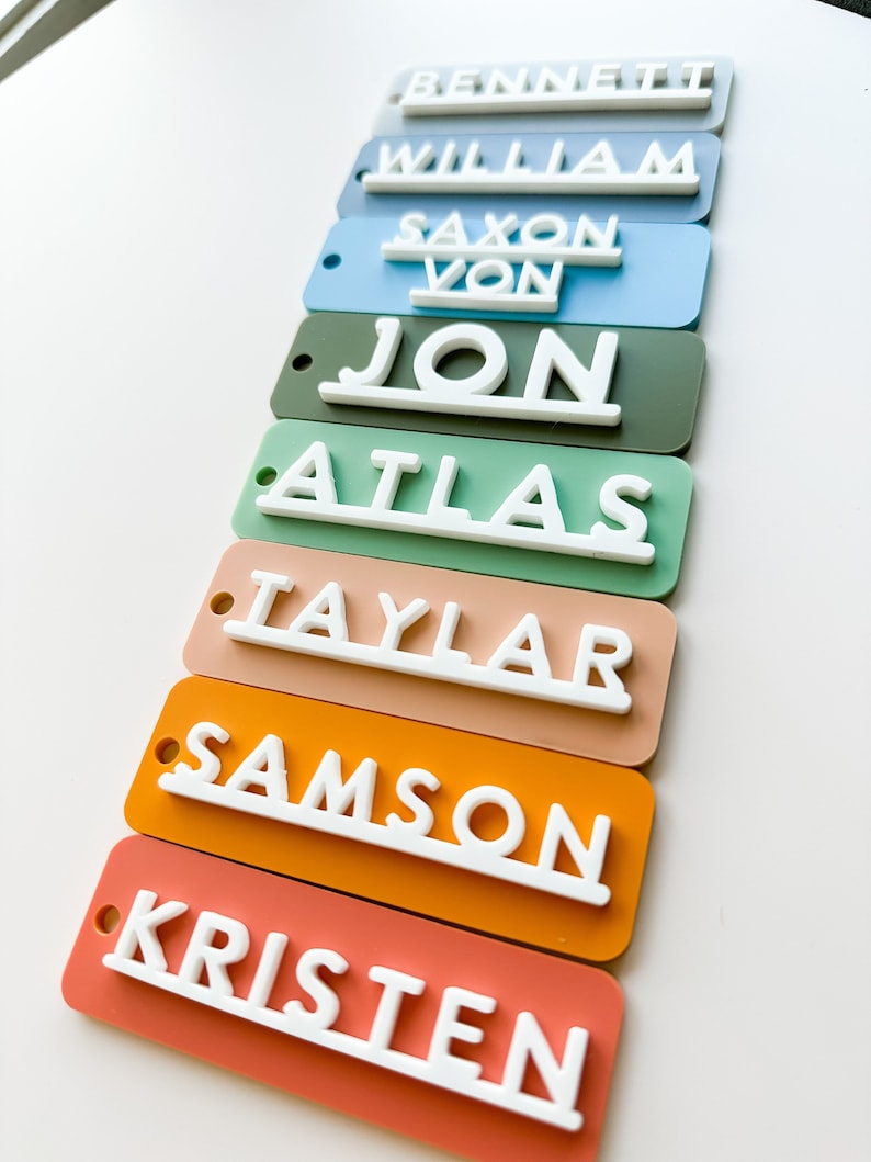 Op de afbeelding: Een set van acht kleurrijke rechthoekige naamstickers met witte letters. De namen zijn: Bennett, William, Saxon Von, Jon, Atlas, Taylar, Samson en Kristen.