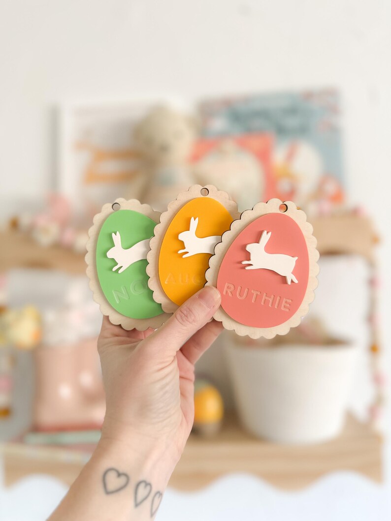 May include: Three wooden Easter egg ornaments with bunny cutouts and names "Nora", "Ava", and "Ruthie" in white lettering.
