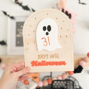 May include: A wooden countdown sign with a white ghost and the number 31. The sign says "Sleeps until Halloween" in orange letters.