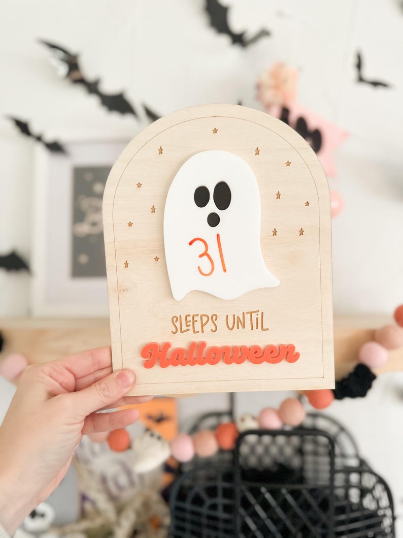 May include: A wooden countdown sign with a white ghost and the number 31. The sign says "Sleeps until Halloween" in orange letters.