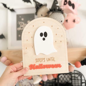 May include: Wooden sign with a white ghost and the text "Sleeps until Halloween" in orange letters. The sign has a light wood background with gold stars.