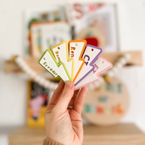 May include: A set of six colorful lightning bolt shaped name tags with the names Freddie, Dominic, Ron, Chris, Henry, and Charlie written in white.