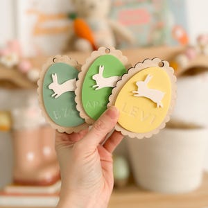 May include: Three wooden Easter egg-shaped ornaments with bunny silhouettes and names "Levi", "Ezra", and "Apollo" written on them.