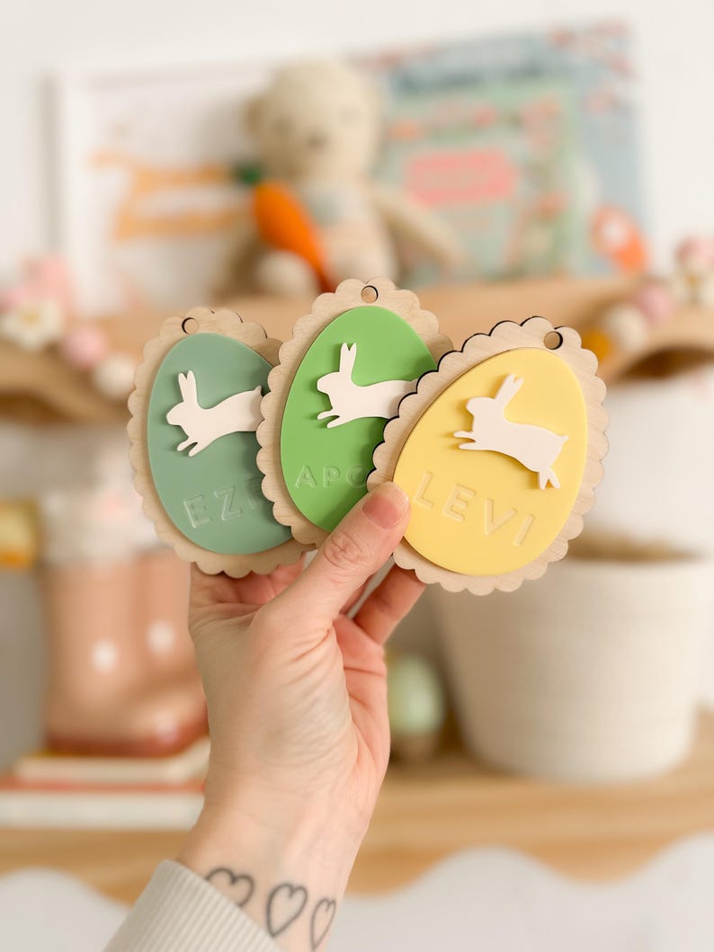 May include: Three wooden Easter egg-shaped ornaments with bunny silhouettes and names "Levi", "Ezra", and "Apollo" written on them.