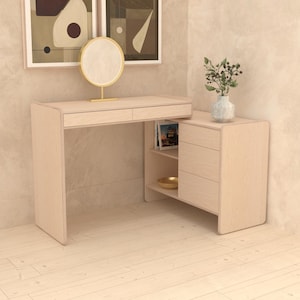 May include: A light wood corner desk with two drawers and a shelf. The desk has a curved edge and is in a room with light wood floors. There are two abstract art prints on the wall above the desk.