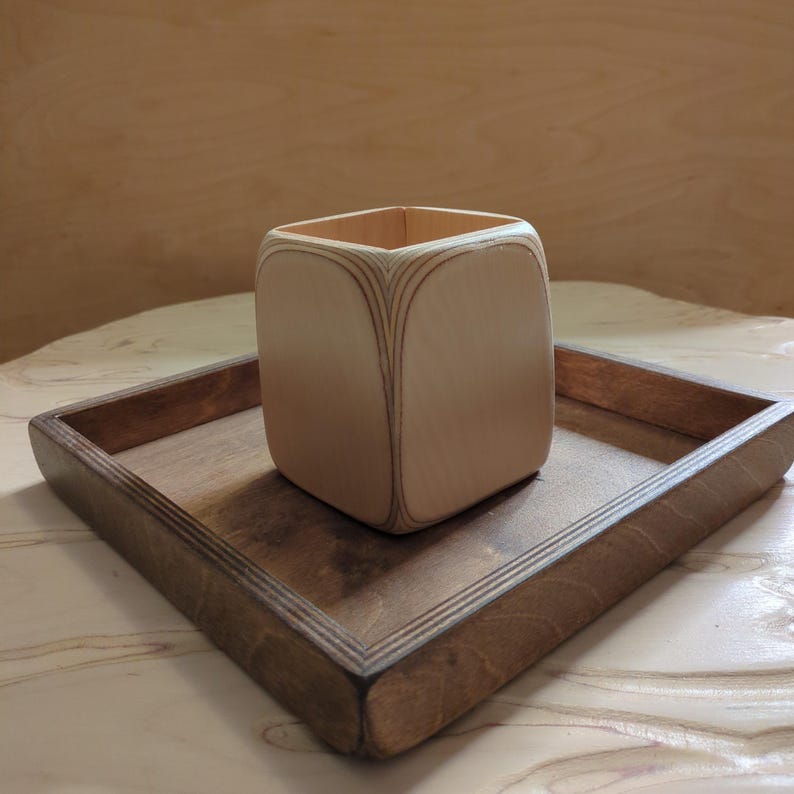May include: A light wood tray with a square, light wood container in the center. The tray has a dark wood border.