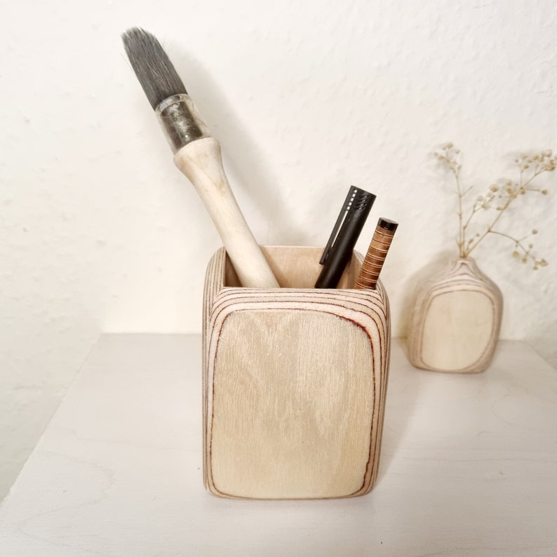 May include: A light wood desktop organizer with a rectangular shape. The organizer has a brush and two pens inside.