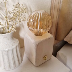 Op de afbeelding: Een houten lampenvoet met een lichtbruine afwerking en een ronde, geribbelde glazen kap. De lamp heeft een gouden schakelaar aan de zijkant.