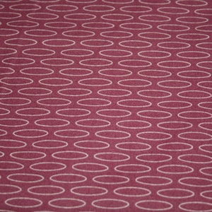 May include: A close-up of a burgundy fabric with a white oval pattern. The fabric has a subtle texture.