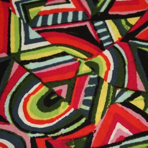 May include: Abstract geometric pattern fabric with a colorful design of red, pink, green, yellow, blue, and black stripes and triangles.