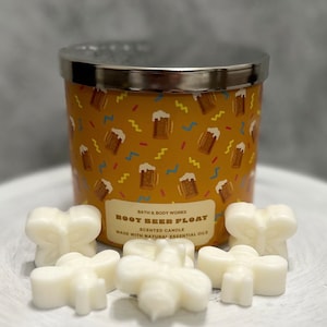 May include: A yellow candle jar with a silver lid and a pattern of beer mugs. The candle is labeled "Root Beer Float" and "Bath & Body Works". The candle is surrounded by six white wax melts shaped like butterflies.