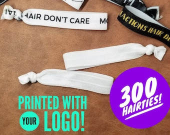 May include: A close-up of a variety of colorful hair ties with different text and logos. The hair ties are arranged on a brown surface. The text on the hair ties includes "The Parlor", "Hair Don't Care", "P/NUP", "de/Art", and "300 Hairties!" The text "Printed with your logo!" is also visible in the image.
