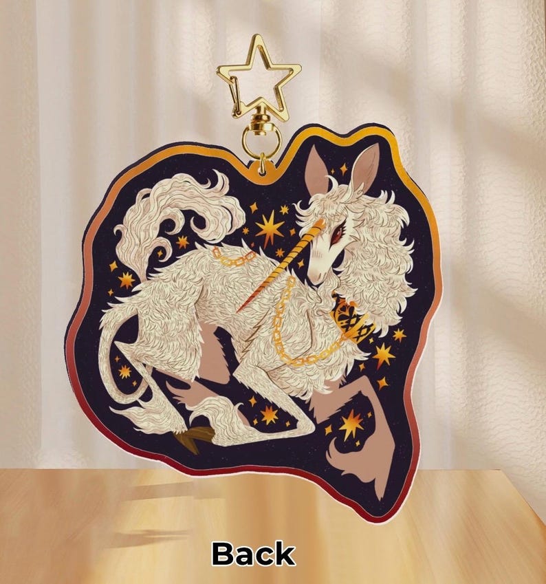 Puede incluir: Un unicornio blanco y esponjoso con un cuerno y una cadena dorados, sobre un fondo azul oscuro con estrellas doradas. El unicornio est&aacute; acostado con la cabeza girada hacia un lado. La imagen est&aacute; en un llavero redondo con borde dorado.