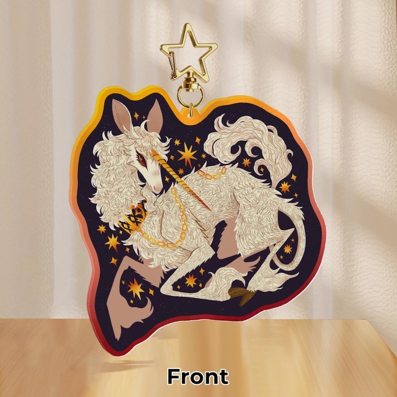 Puede incluir: Un llavero de acr&iacute;lico duradero que representa un unicornio blanco con un cuerno y una cadena dorados, rodeado de estrellas sobre un fondo azul oscuro. El unicornio est&aacute; enroscado en una posici&oacute;n de sue&ntilde;o. El llavero tiene un anillo de metal dorado.