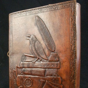 Könnte beinhalten: Ein braunes Lederjournal mit einem geprägten Raben, einer Feder und Büchern. Das Cover-Design umfasst einen fünfzackigen Stern und einen dekorativen Rand. Das Journal wird mit einem Metallverschluss gesichert und hat eine detaillierte, strukturierte Oberfläche.