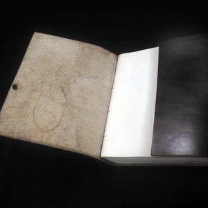Pode incluir: Um di&aacute;rio aberto com uma capa de couro marrom e uma p&aacute;gina branca em branco. O interior da capa &eacute; de couro marrom claro.